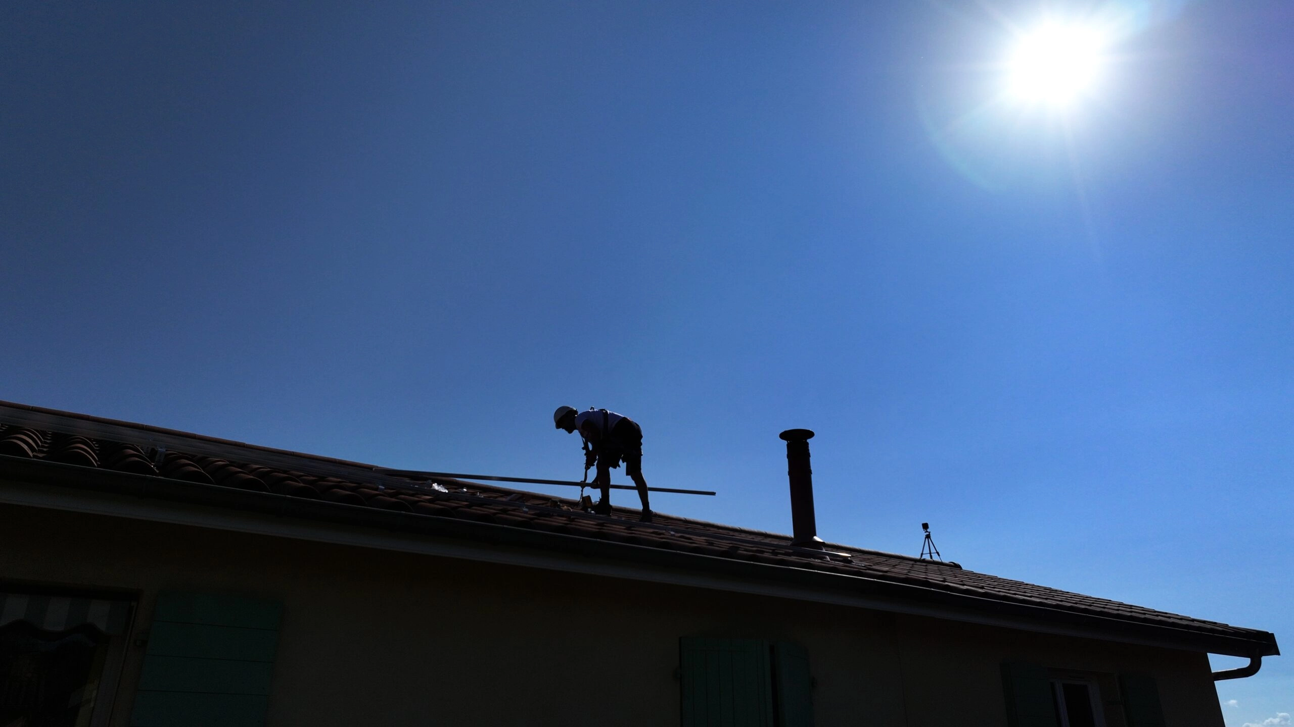 Technicien à contre jour installant des panneaux solaires photovoltaïques sur le toit d'une maison
