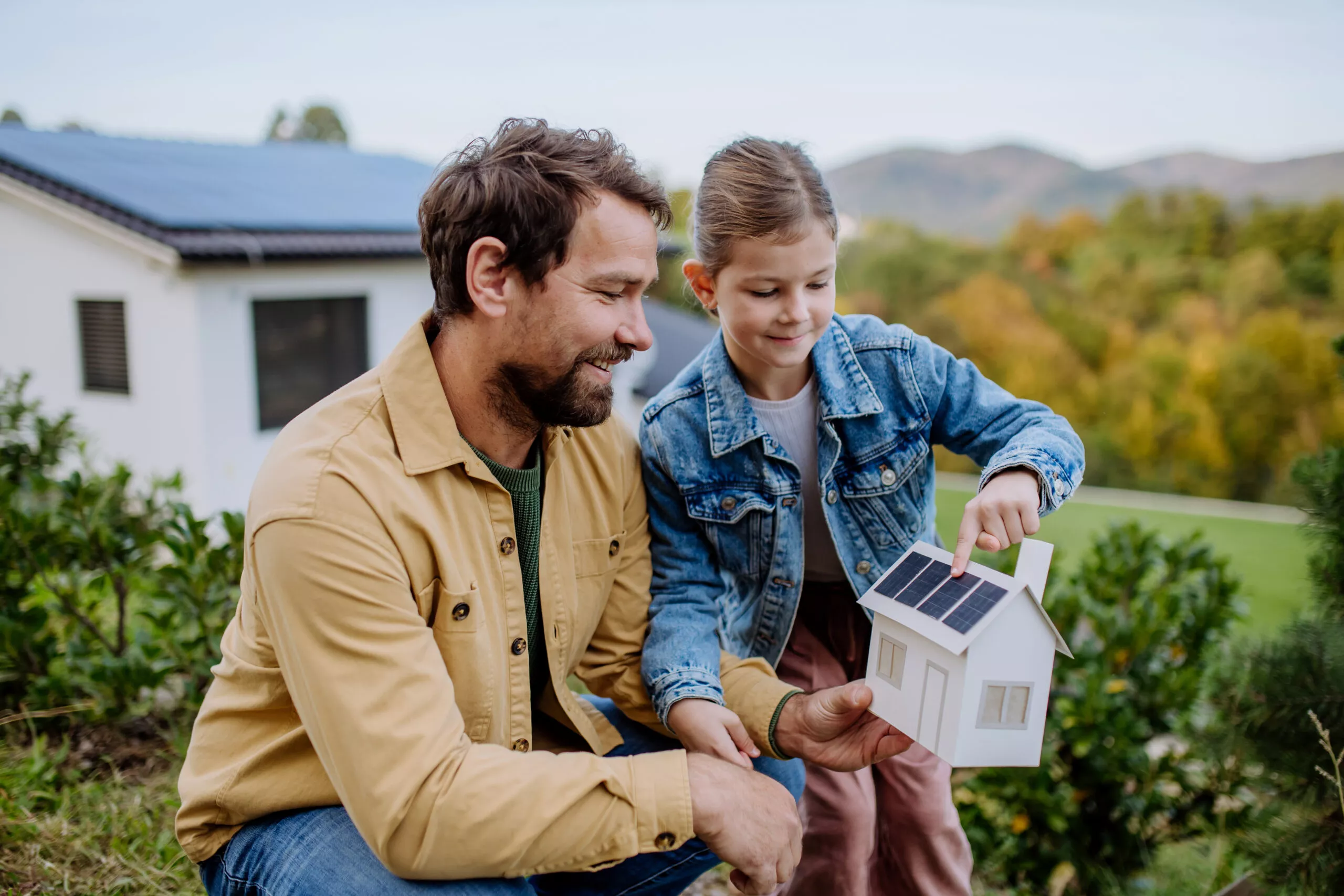 Un père et sa fille tenant une maison avec des panneaux solaires photovoltaïques