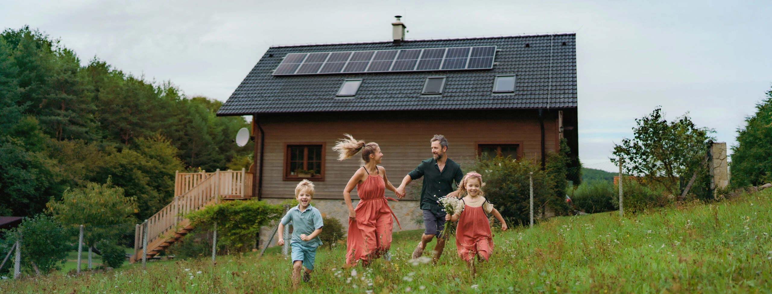 Famille heureuse courant près de sa maison équipée de panneaux solaires. Concept d'énergie alternative, d'économie de ressources et de mode de vie durable.