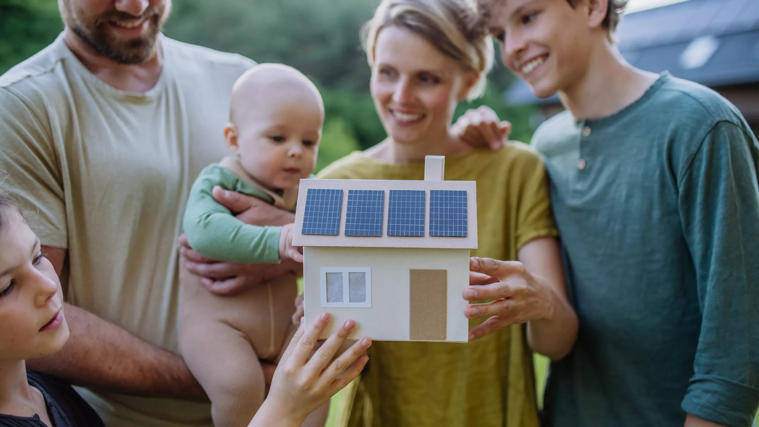 Famille heureuse avec trois enfants tenant une maquette de maison équipée de panneaux solaires photovoltaïques. Concept d'énergie alternative, d'économie de ressources et de mode de vie durable