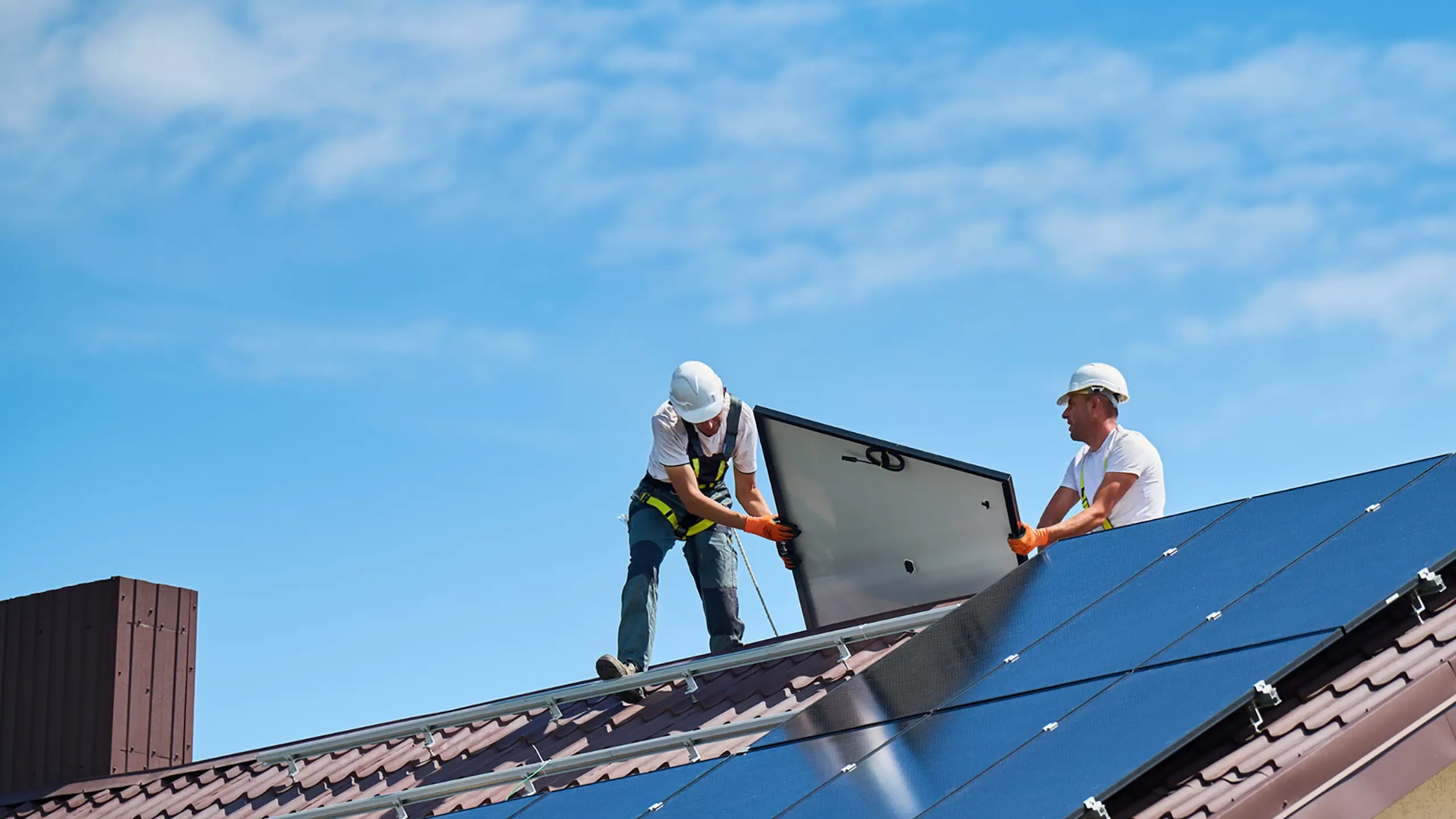 Deux experts avec des équipements posent des panneaux solaires photovoltaïque sur le toit d'une belle maison